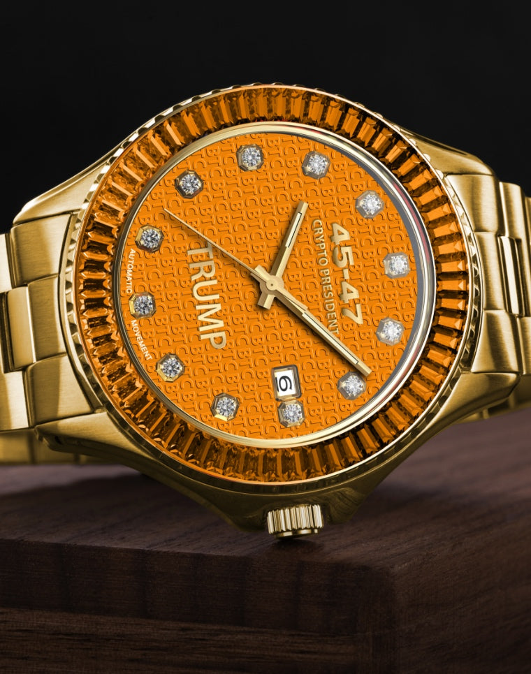 Gold Trump wristwatch with orange face, diamond hour markers, and engraved text on bezel.