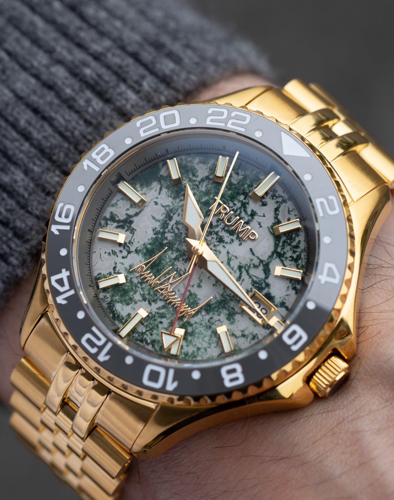 Gold Trump wristwatch with green marble dial, black bezel, and gold bracelet on wrist.