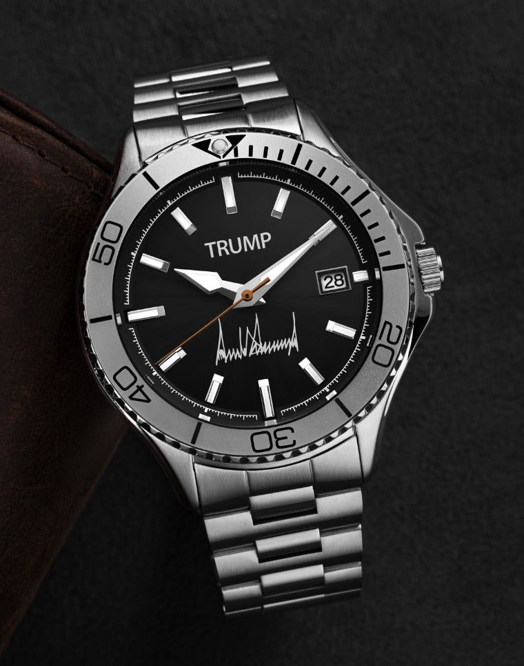 Silver Trump wristwatch with black dial, date display, and engraved signature on dark background.