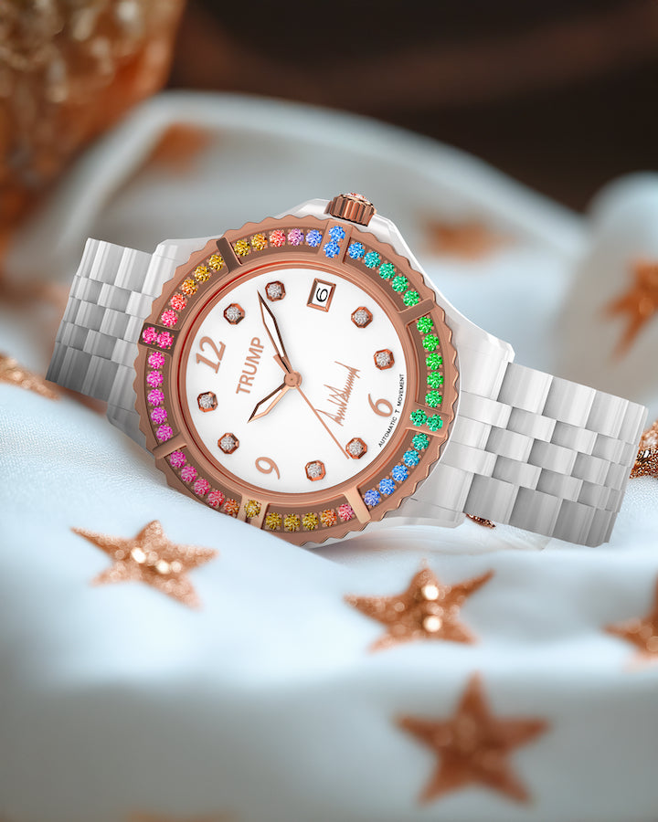 White luxury watch with rose gold bezel, rainbow gems, and TRUMP branding on satin star cloth.