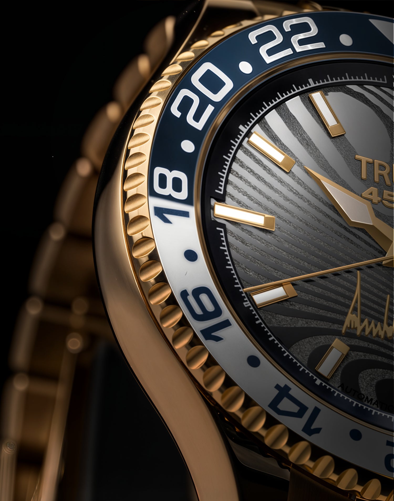 Close-up of luxury gold wristwatch with black bezel, wave-pattern dial, and luminous hour markers.
