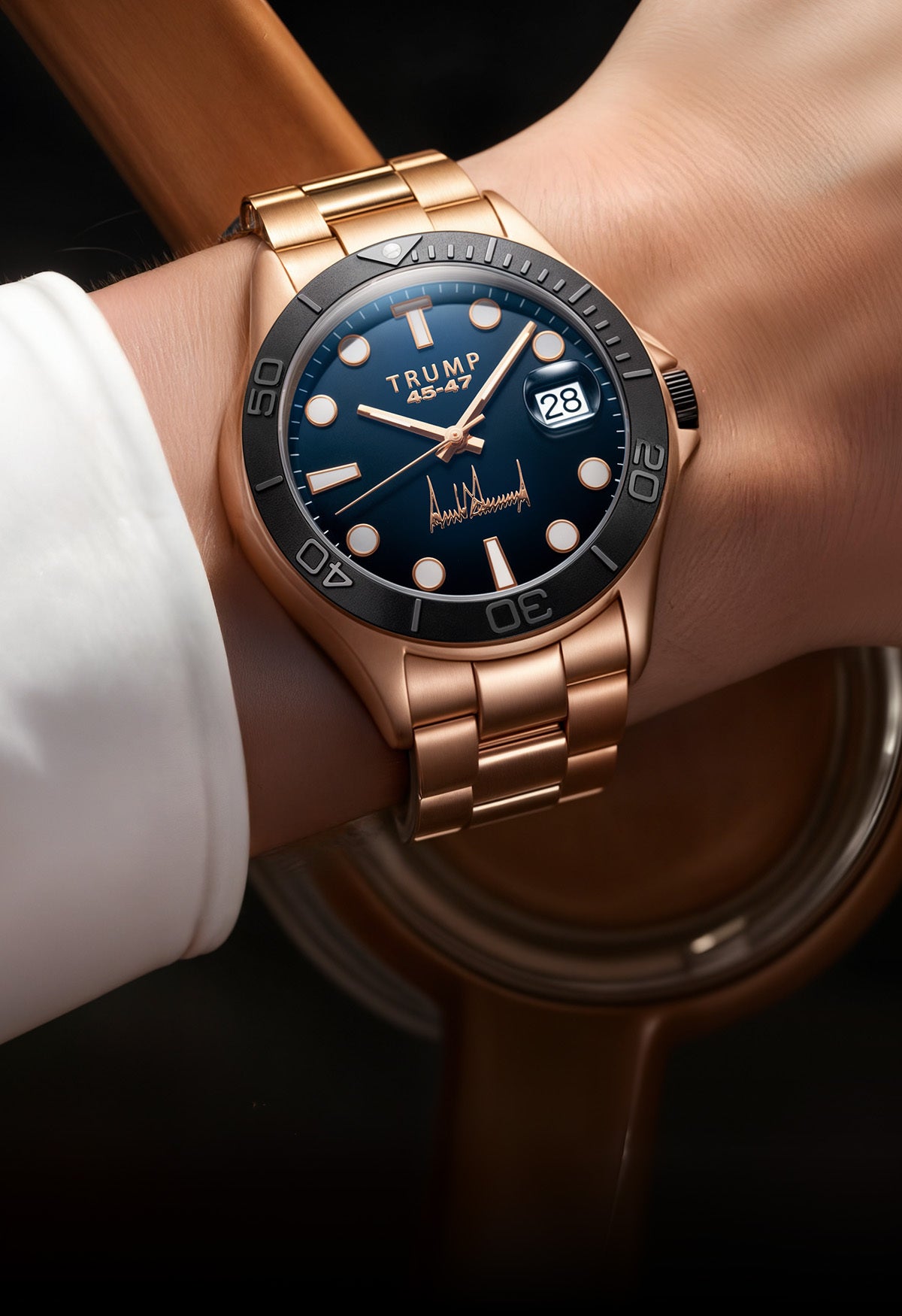Gold wristwatch with black bezel, blue dial, Trump branding, date window, and metal bracelet.