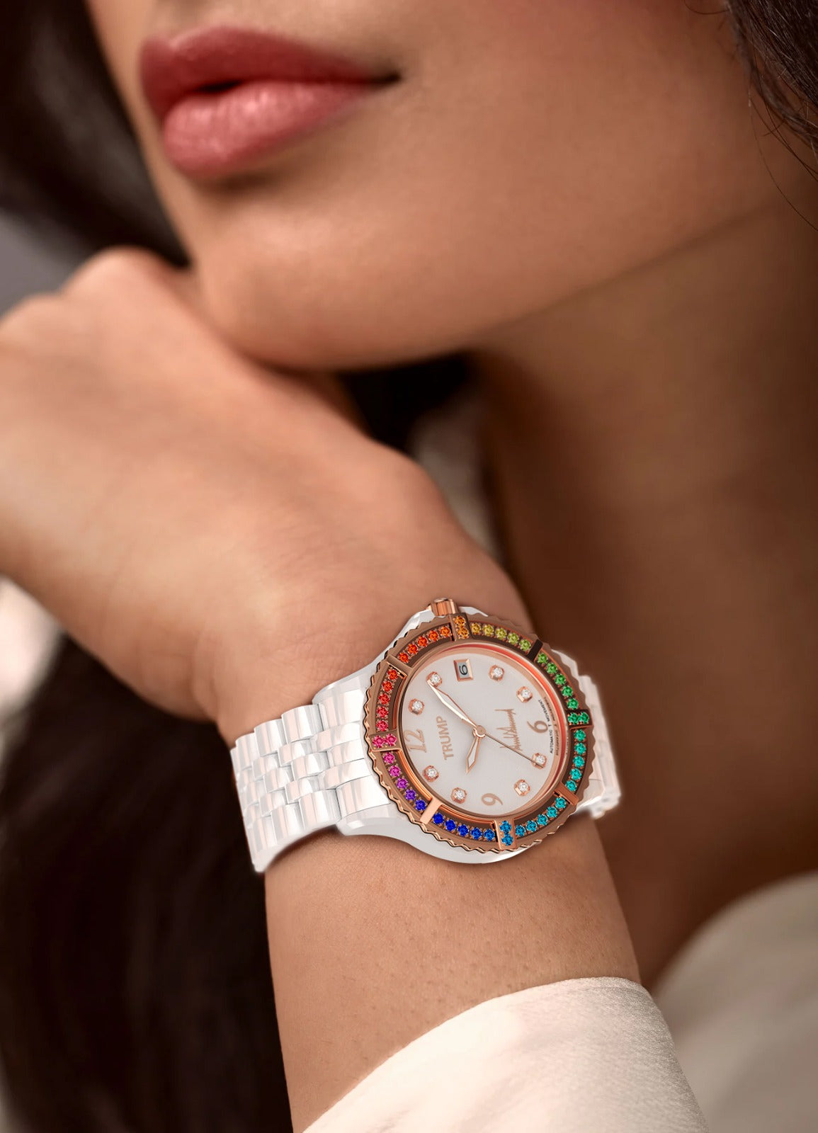 White ceramic wristwatch with rainbow gemstone bezel and diamond markers on woman's wrist.